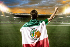 hombre-alentando-a-la-seleccion-mexicana-en-estadio-de-futbol-con-la-bandera-en-su-espalda-bandera-de-mexico-soccer-estadio-1.jpg